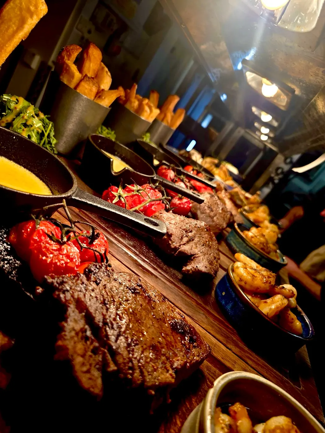 Steaks with roasted tomatoes and bowls of chips on a table